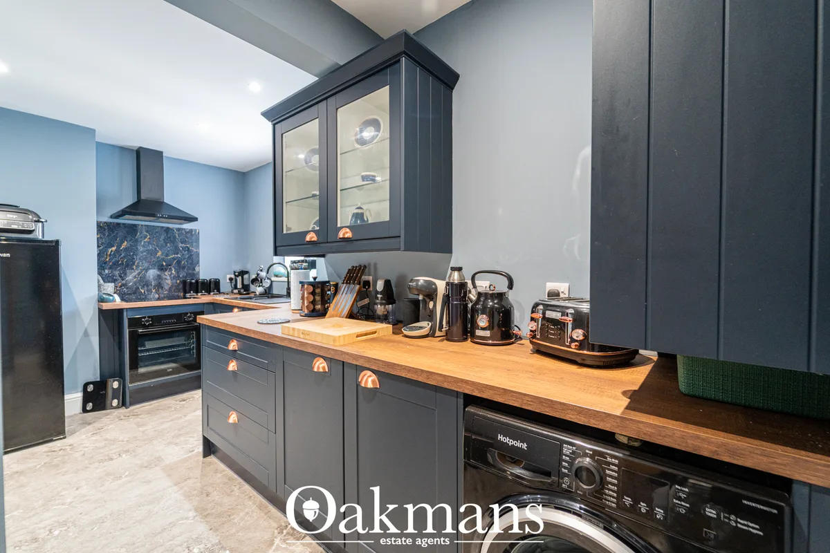 Modern kitchen with charcoal cabinetry, wooden worktops, black appliances, glass-fronted wall units, and copper hardware