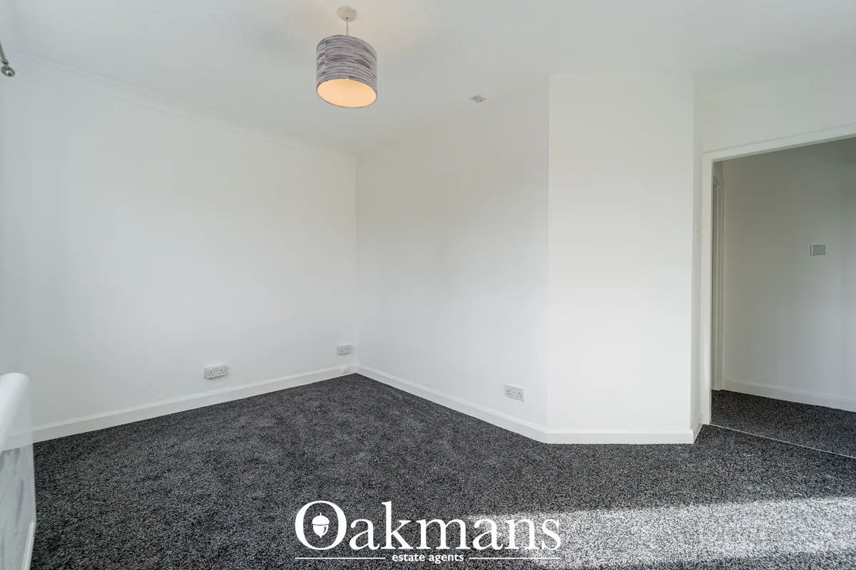 Empty hallway with white walls, dark carpet, pendant light fixture, electrical outlets, and doorway to adjacent room