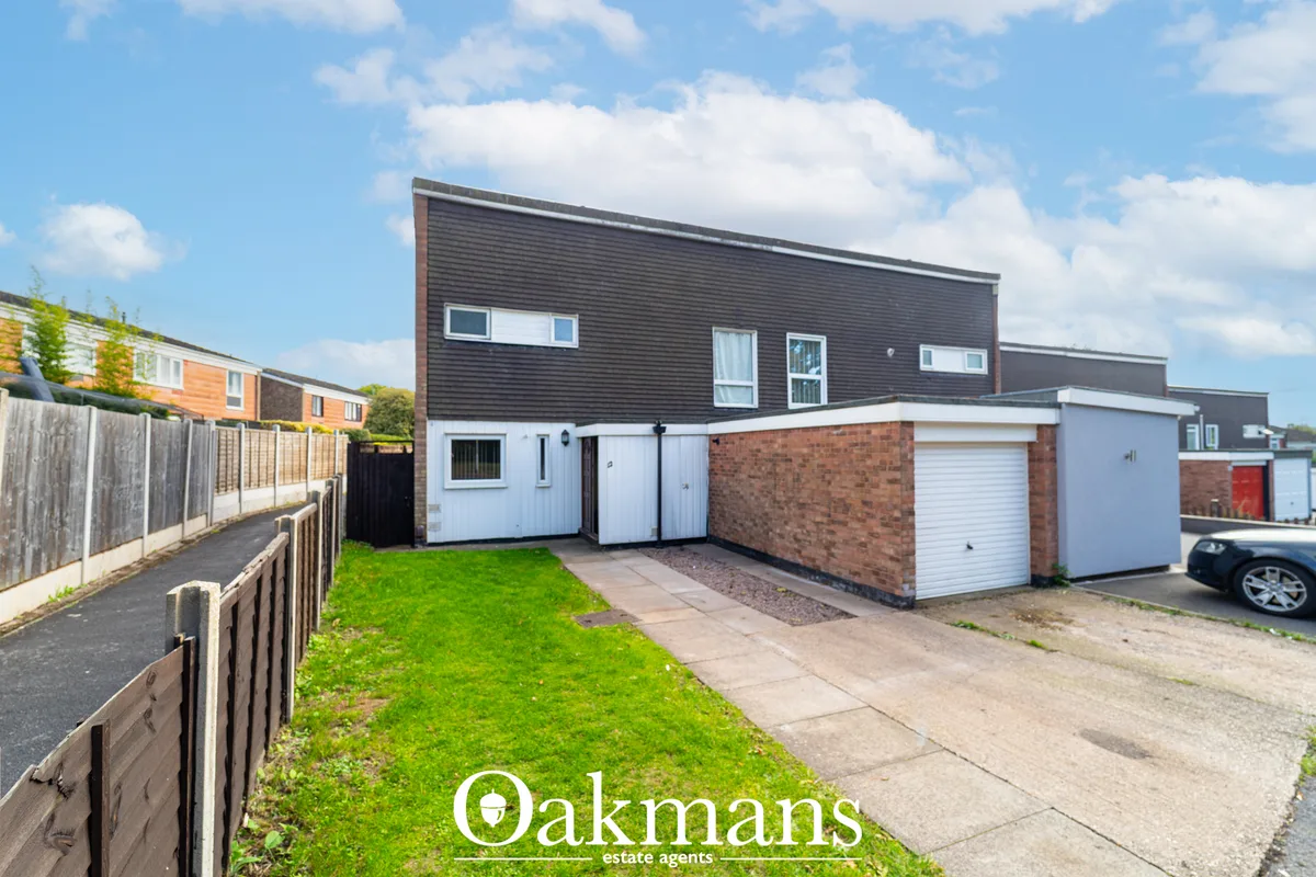Front view of a modern two-storey house with dark upper cladding, brick base, white garage door, paved driveway and gree