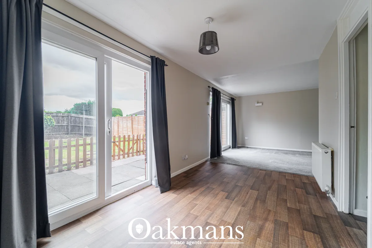 Spacious living room with wooden flooring, patio doors opening to garden, black curtains, pendant light, and neutral déc