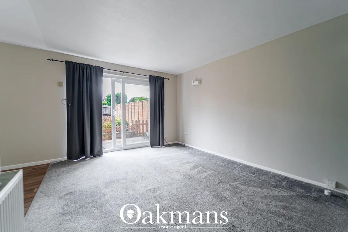 Spacious living room with grey carpet, beige walls, white ceiling, dark curtains at patio doors opening to garden with d