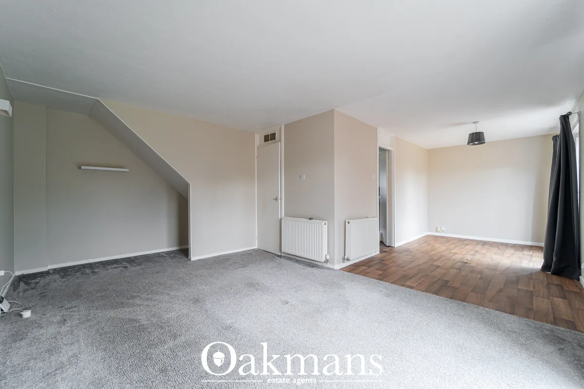 Spacious living room with cream walls, carpeted and wooden flooring, radiators, staircase to left, multiple doors and wi