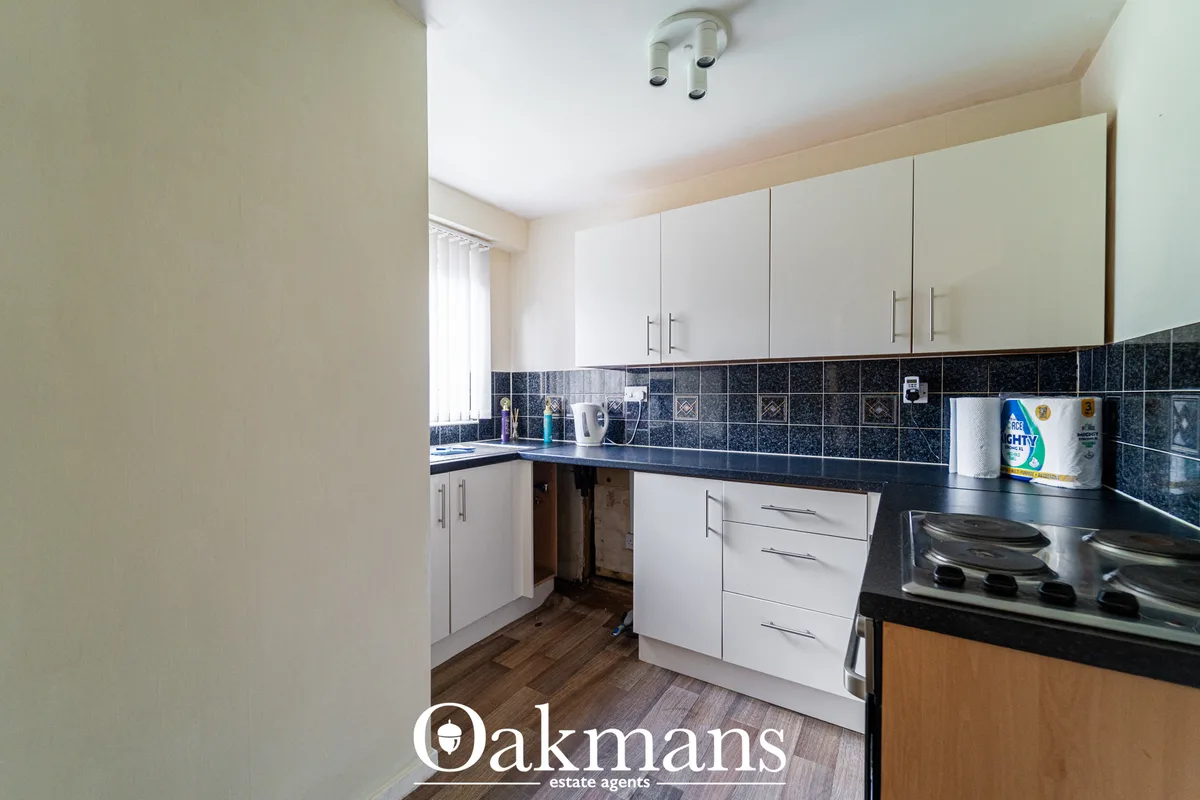 Fitted kitchen with white wall and base units, black granite worktops, dark tile splashback, electric hob, window with b