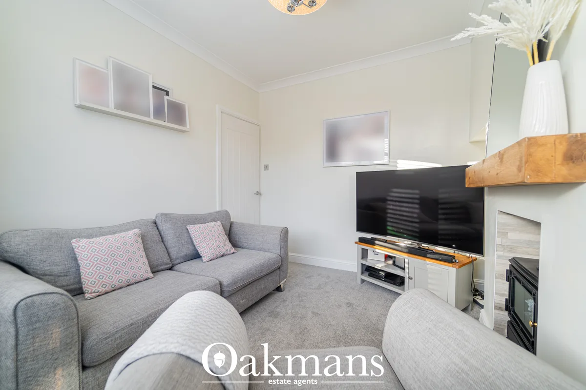Bright living room with grey corner sofa, patterned cushions, wall-mounted TV above wooden media unit, and fireplace