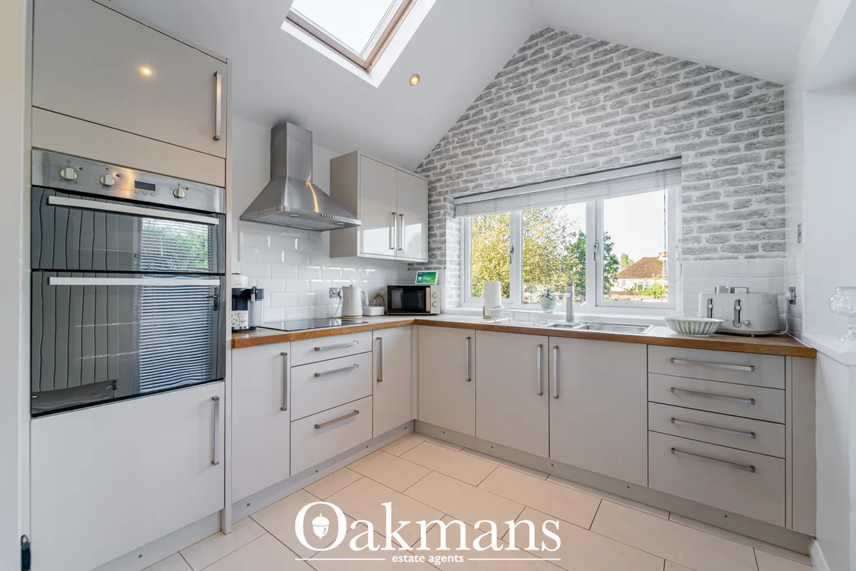 Modern kitchen with cream cabinetry, wood worktops, stainless steel appliances, exposed brick wall, skylight and garden 