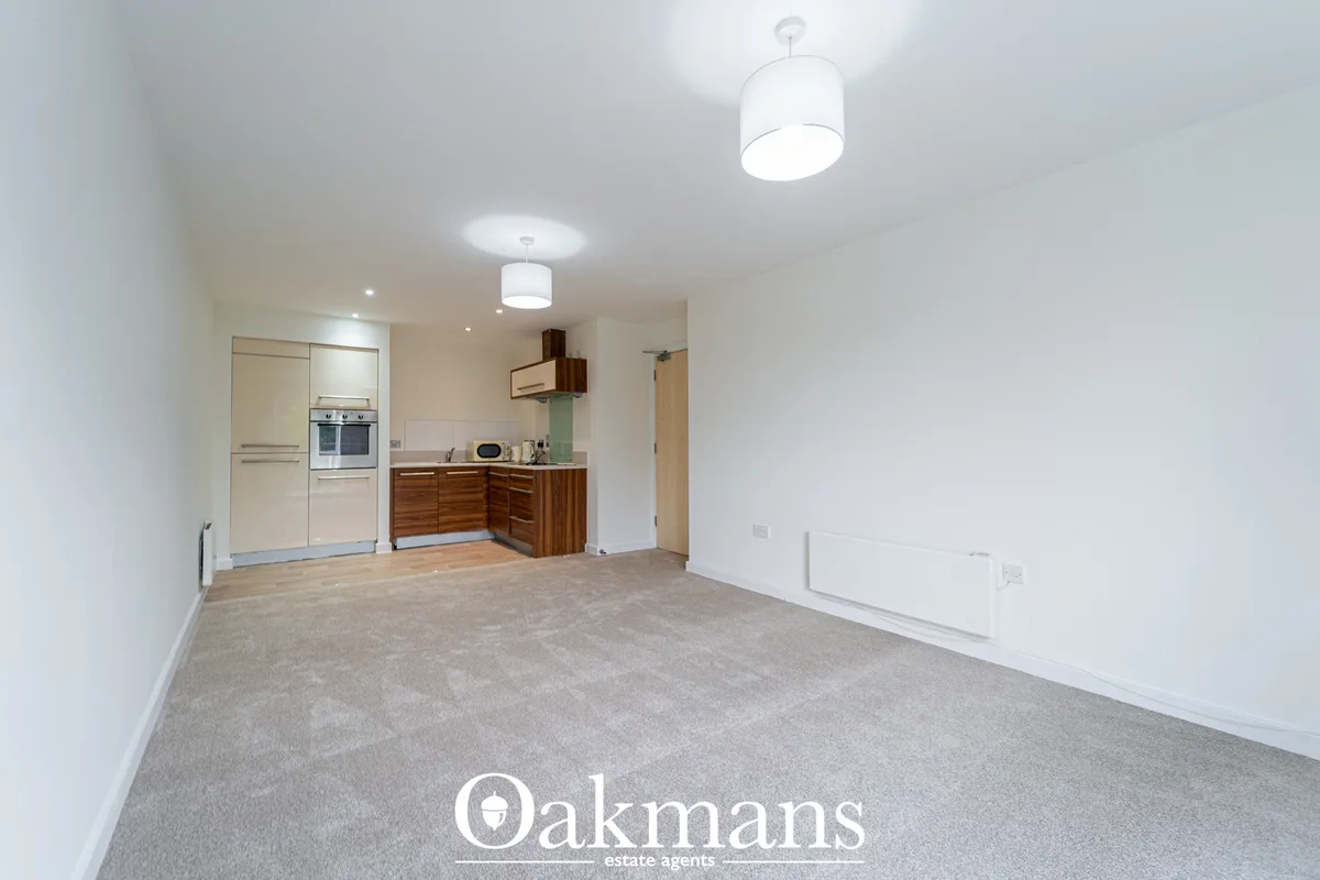 Open-plan kitchen with cream and walnut units, built-in ovens, grey carpet, pendant lights and breakfast bar