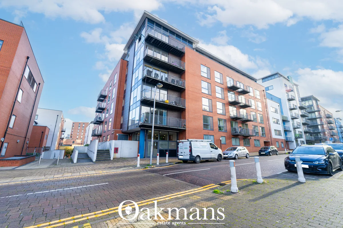 Modern brick apartment building with balconies, ground-floor entrance with blue door, parked vehicles, paved courtyard a