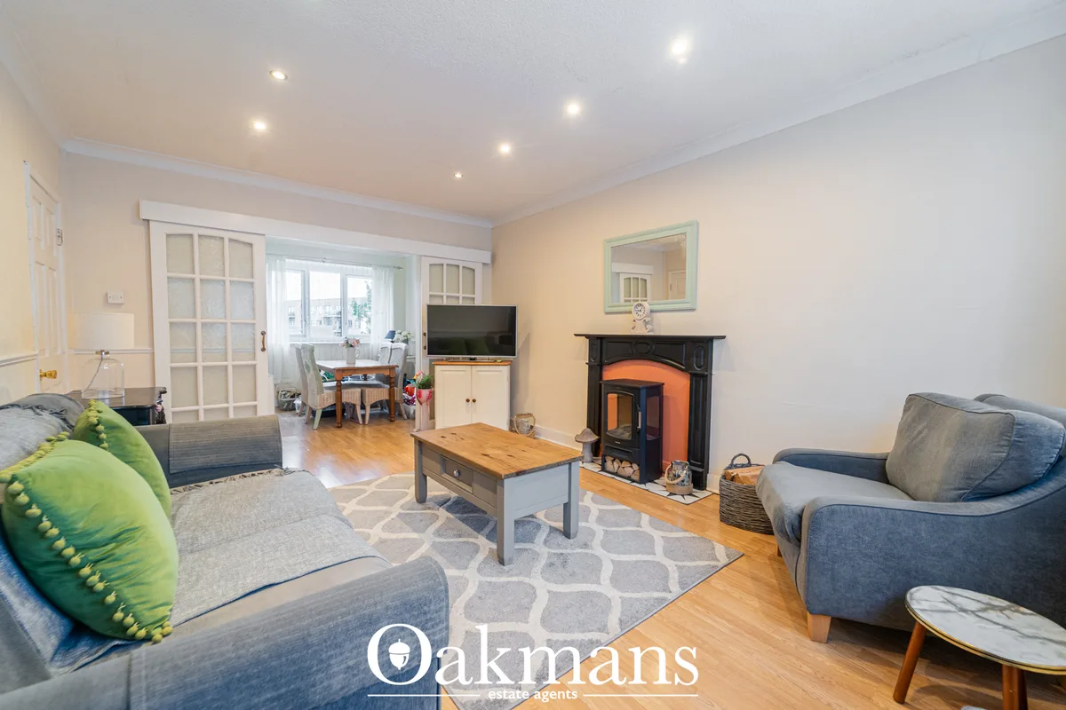 Bright living room with wooden flooring, grey sofas with green accent cushion, wood-burner stove with orange insert, woo