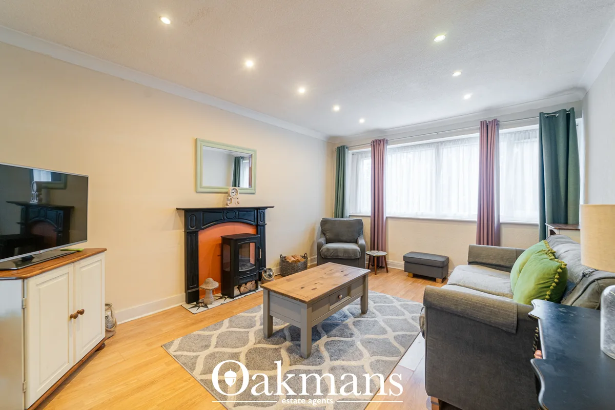 Spacious living room with wooden flooring, cream walls, fireplace with orange stove, two sofas, coffee table, TV unit, a