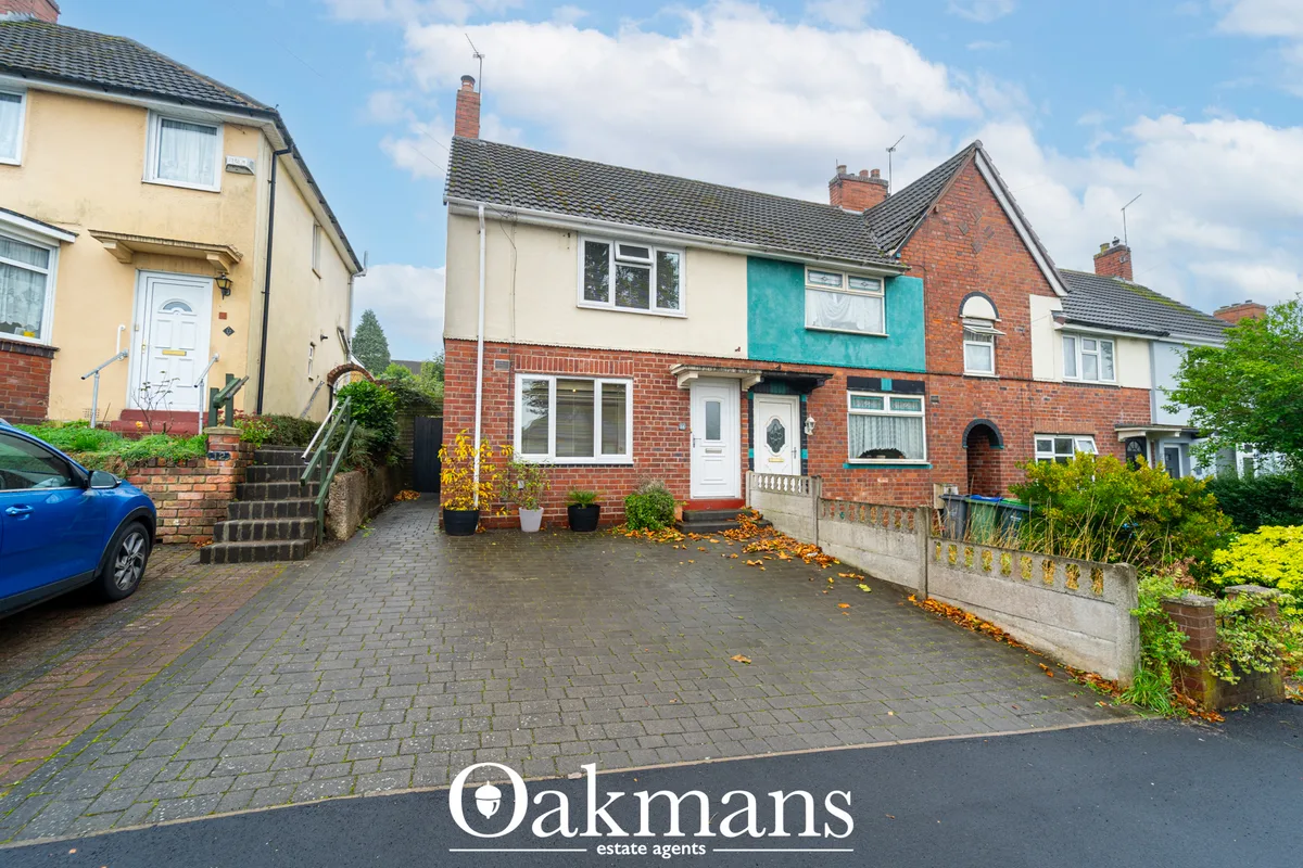 Semi-detached brick house with cream render upper storey, turquoise accent panel, driveway and front garden with stone w
