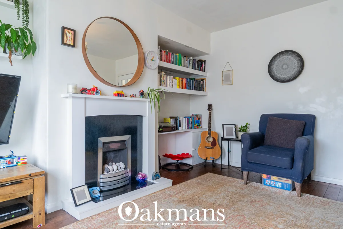 Bright living room with fireplace, round wooden mirror, built-in shelving, blue armchair, acoustic guitar, wooden floori