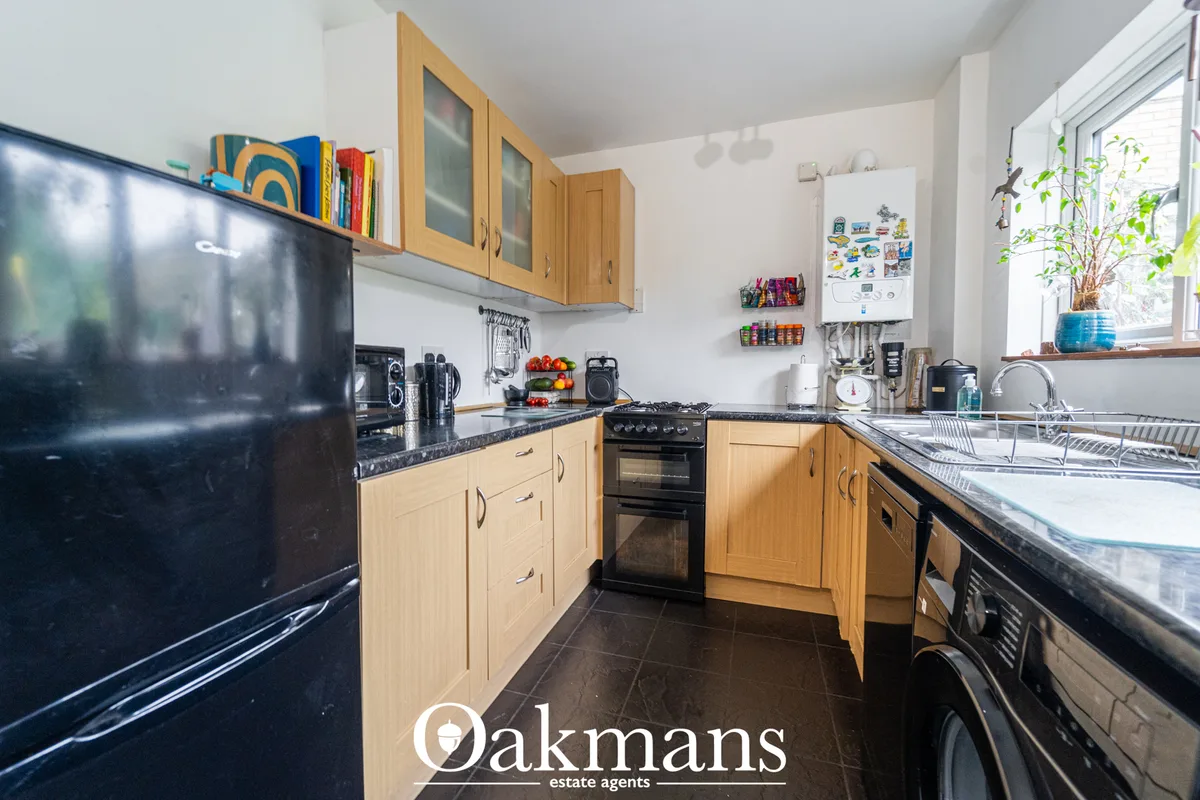 Modern fitted kitchen with wooden units, dark granite worktops, black appliances, and bright windows overlooking garden 