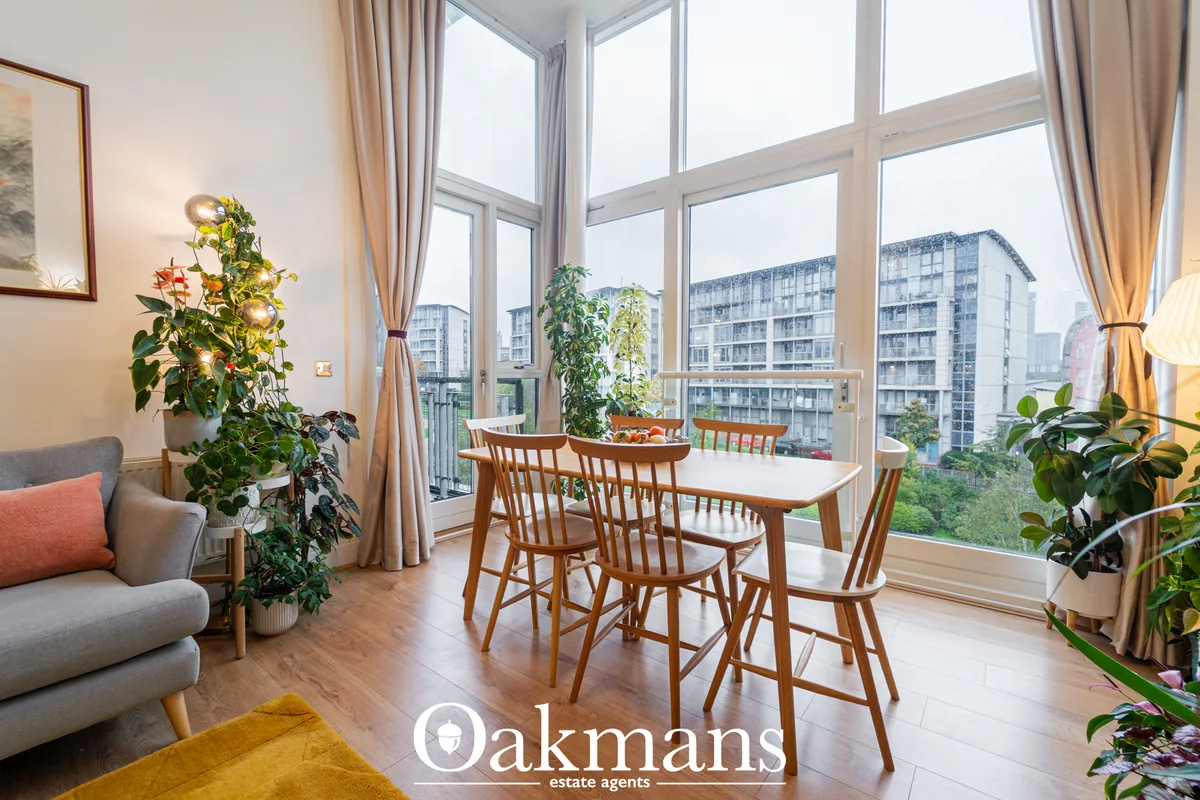 Modern dining room with wooden table and chairs, floor-to-ceiling windows overlooking city buildings, indoor plants, gra