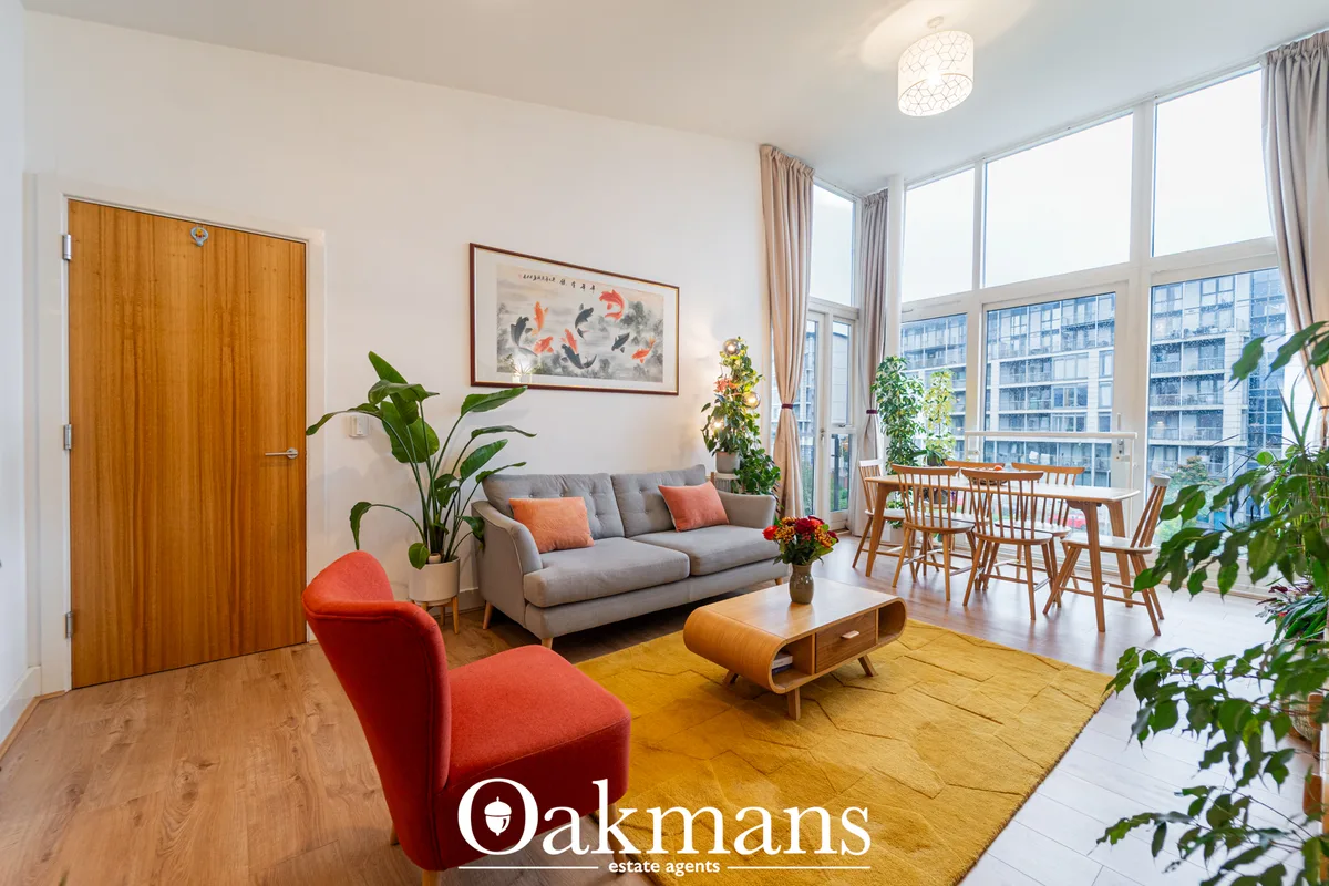 Bright open-plan living room with grey sofa, red accent chair, wooden coffee table, large windows overlooking city, pott