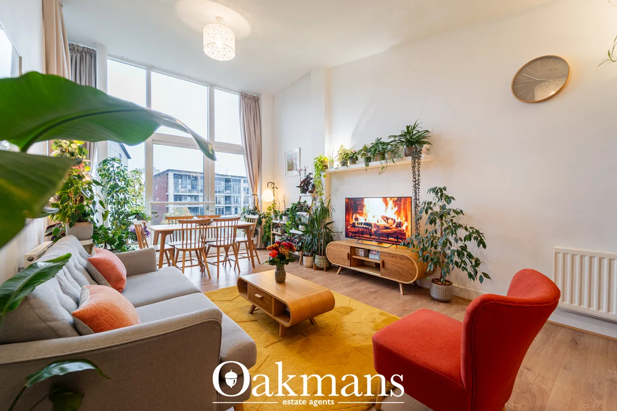 Bright modern living room with grey sofa, red armchair, wooden coffee table, plants, and TV on wooden unit. Large window