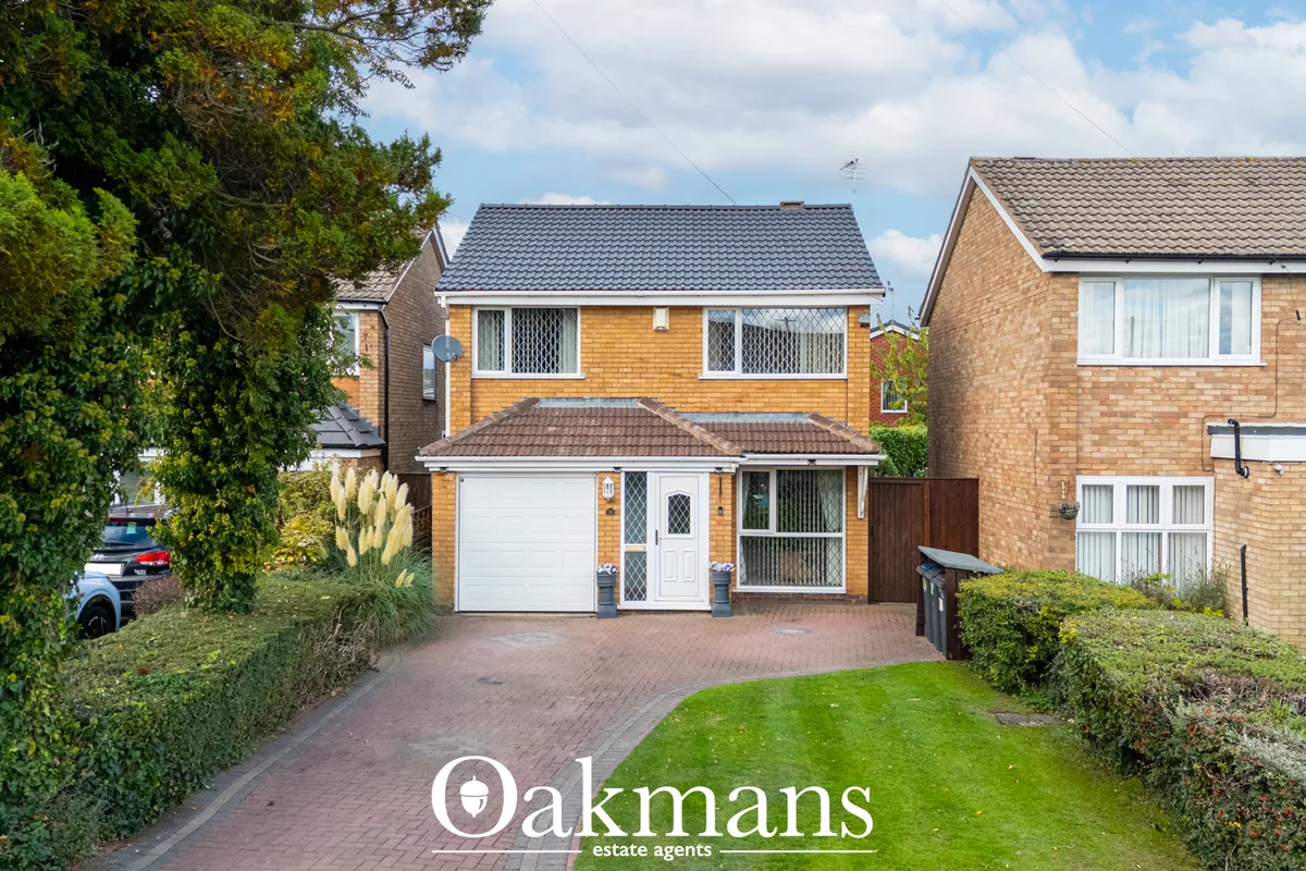 Two-storey brick detached house with white garage door, brick driveway, manicured front garden and neighbouring properti
