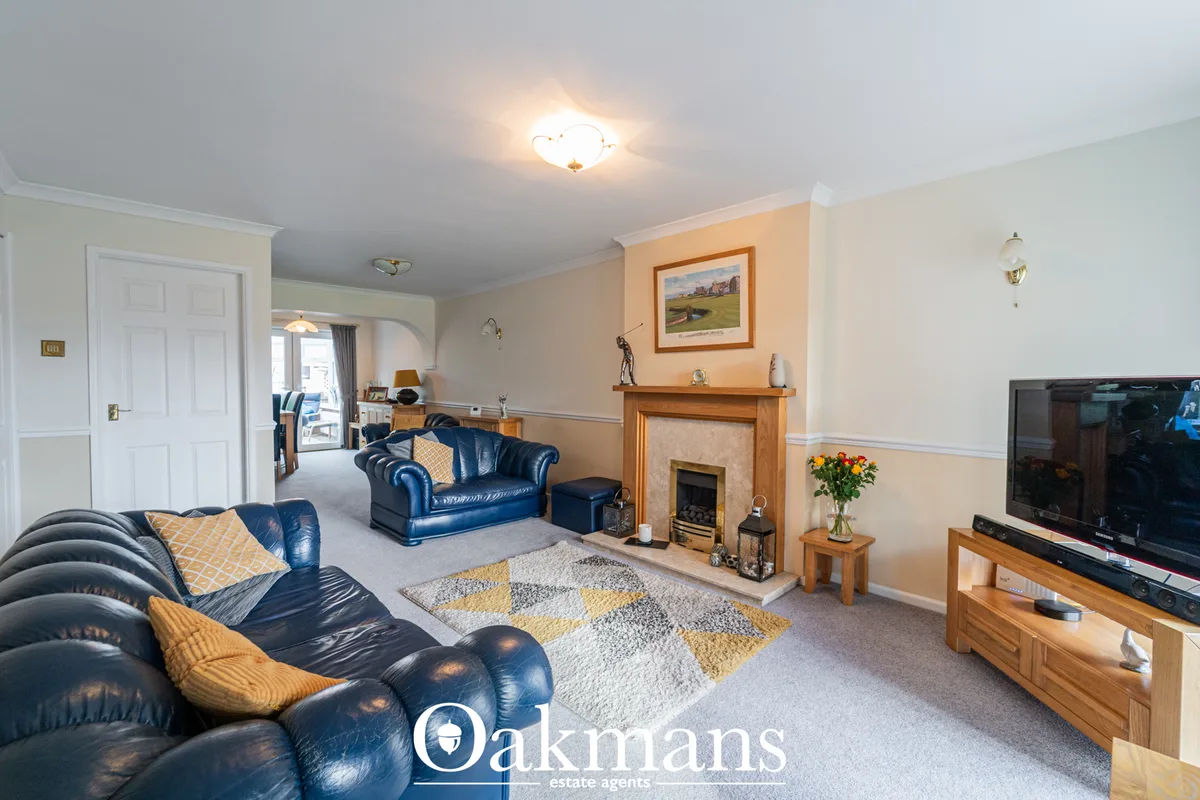 Spacious living room with blue leather Chesterfield sofas, fireplace with wooden surround, TV, patterned rug, and peach 