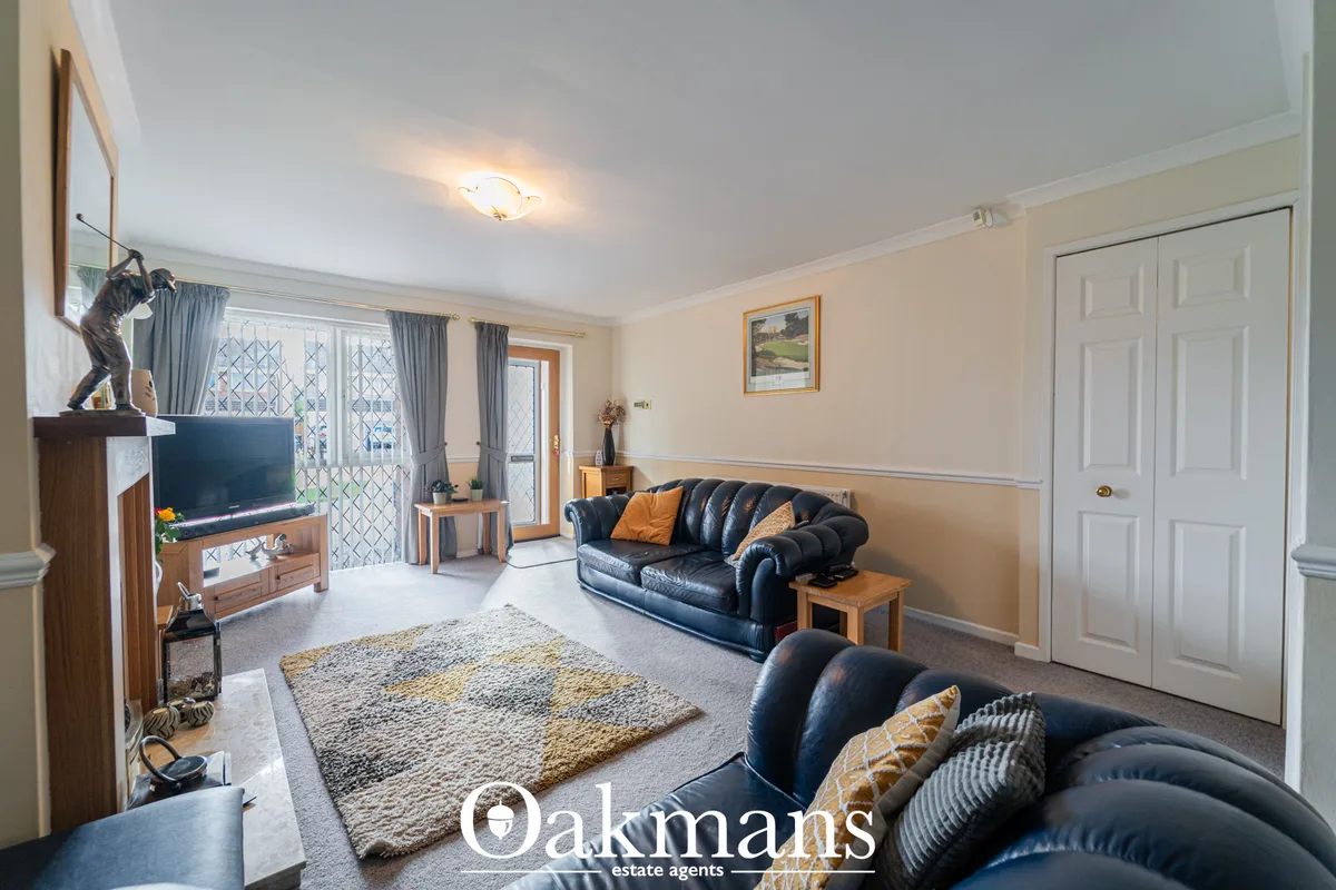Spacious living room with two black leather sofas, patterned rugs, fireplace, TV on wooden stand, and patio doors with g
