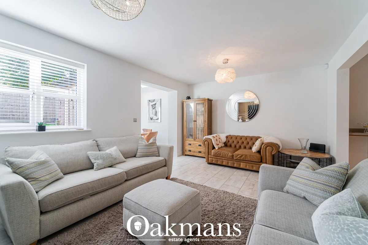Bright open-plan living room with grey sofas, tan leather Chesterfield sofa, wooden furniture, decorative wall art, pend