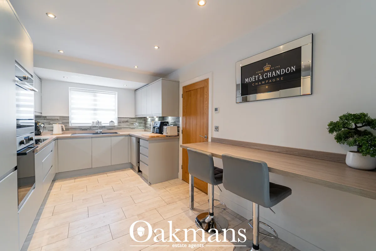 Modern white fitted kitchen with wooden worktops, breakfast bar seating, tiled flooring and Moët & Chandon advertising s