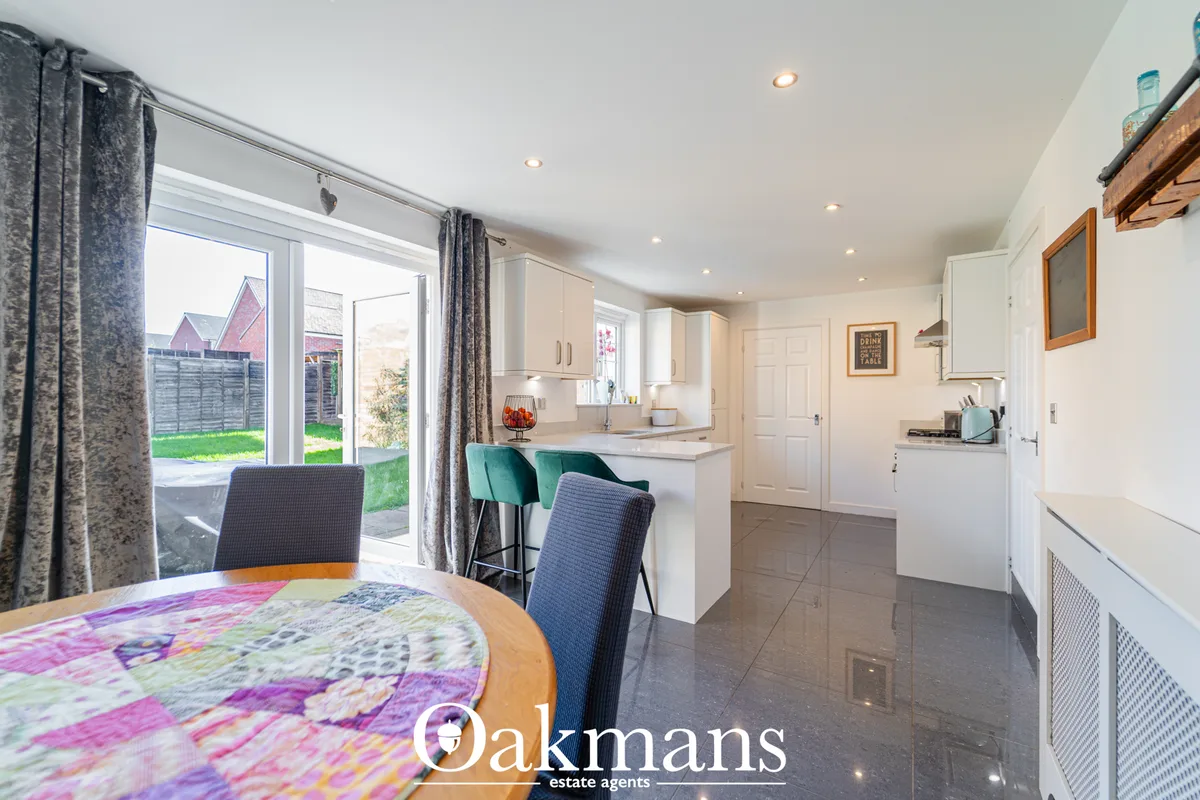 Modern open-plan kitchen with white fitted units, breakfast bar with teal bar stools, grey tiled flooring, and patio doo