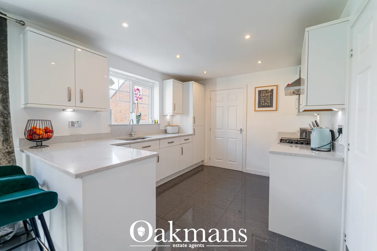 Modern fitted kitchen with white units, grey granite worktops, breakfast bar, gas hob, integrated appliances and dark ti