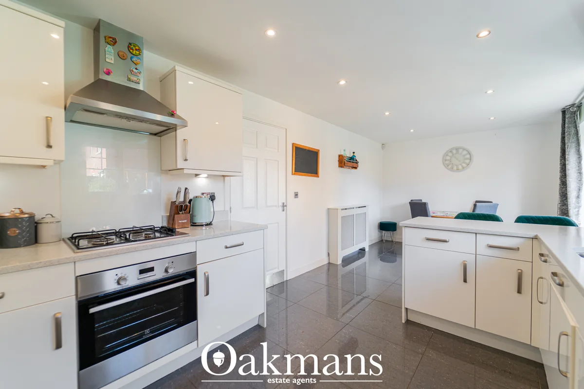 Modern fitted kitchen with white units, stainless steel cooker, breakfast bar, and open-plan dining area with teal seati