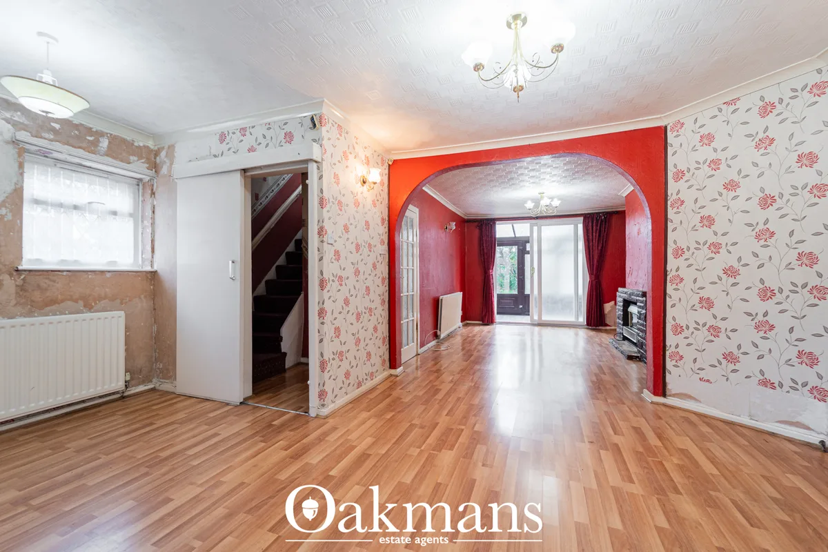 Spacious living room with wooden flooring, floral wallpaper, red decorative archway, bay window with curtains and firepl