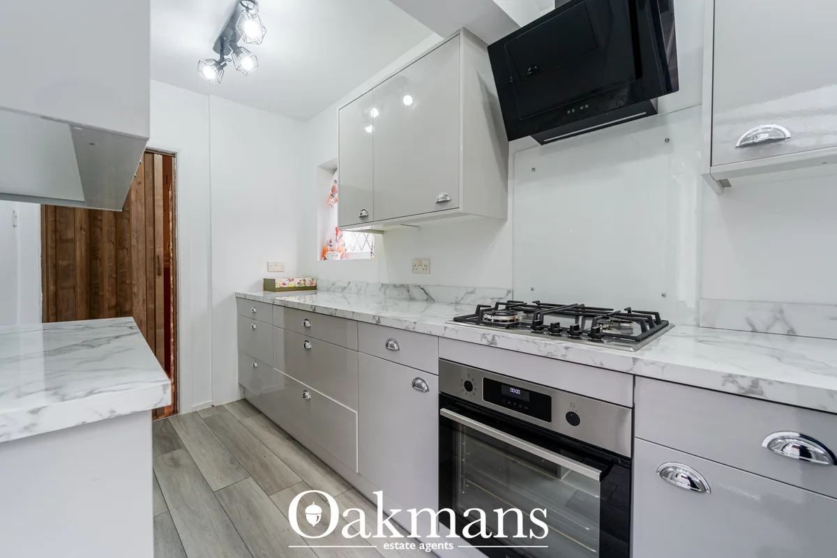 Modern fitted kitchen with white gloss units, marble worktops, gas hob, built-in oven, wall-mounted TV and stainless ste