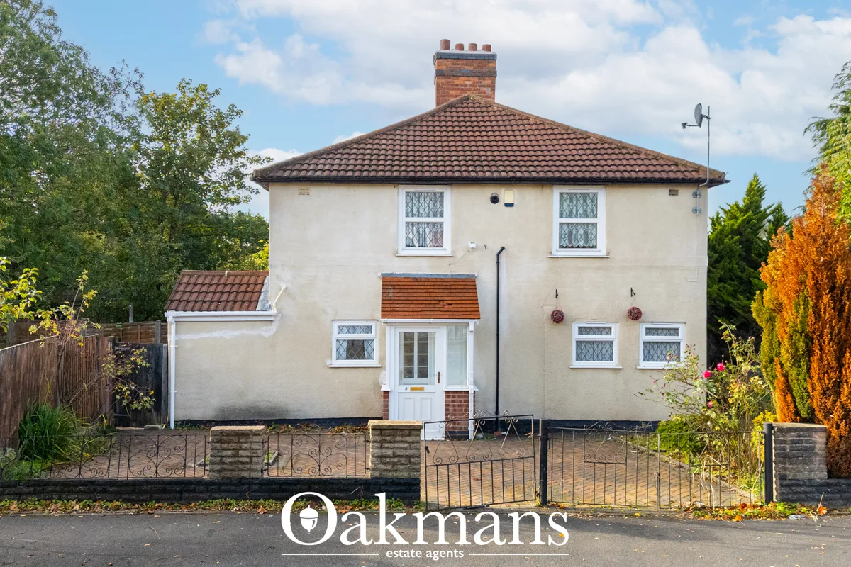Two-storey cream rendered house with hipped tile roof, brick chimney, white windows, central entrance porch, mature hedg