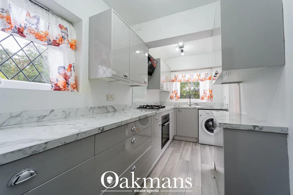 Modern galley kitchen with grey cabinetry, marble worktops, gas hob, built-in oven, washing machine, white metro tiles, 