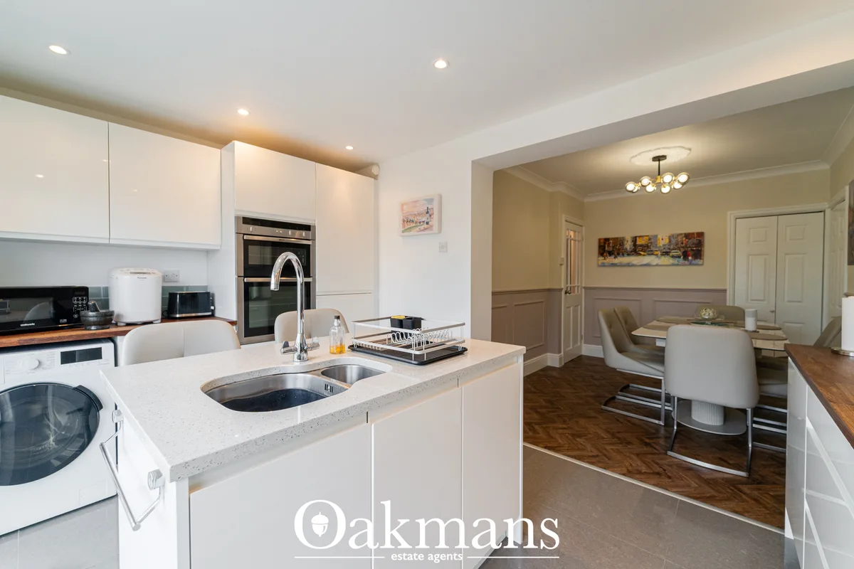 Modern fitted kitchen with white cabinetry, grey worktops, double sink with chrome tap, built-in oven, and open-plan vie