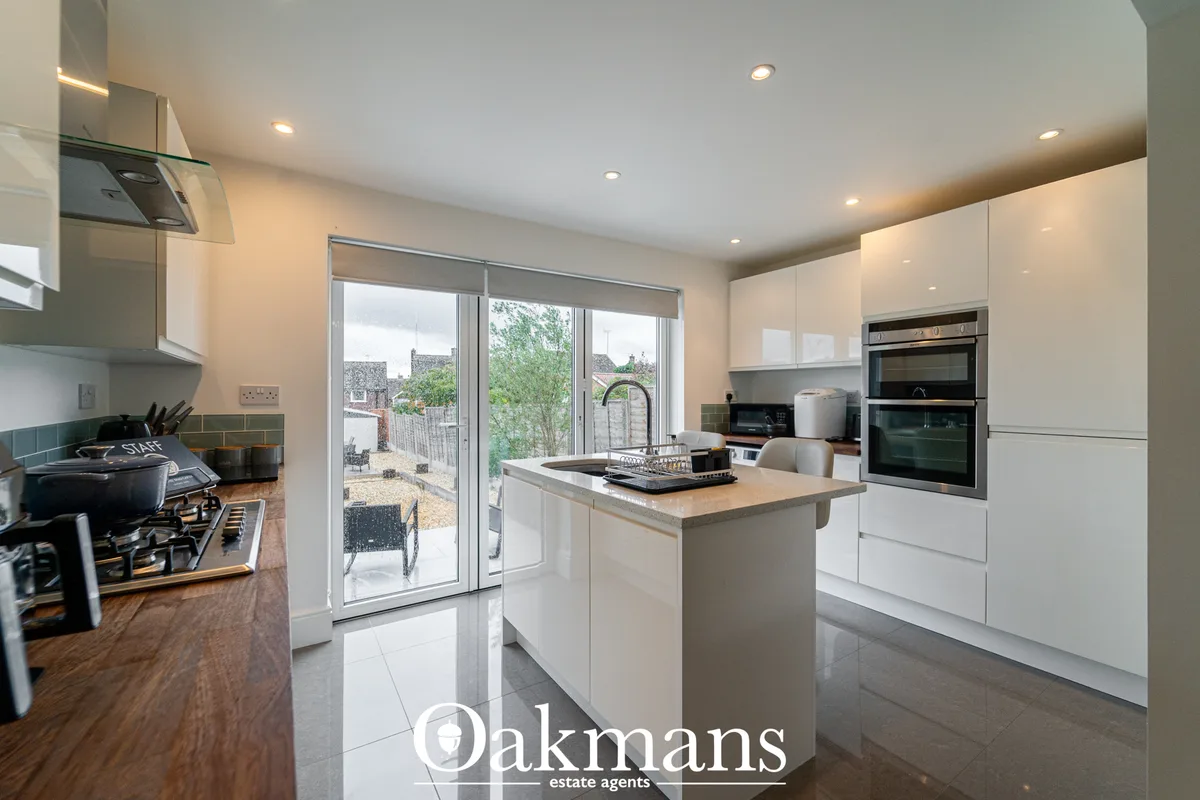 Modern white fitted kitchen with island, gas hob, integrated appliances, sliding doors to garden, recessed lighting and 