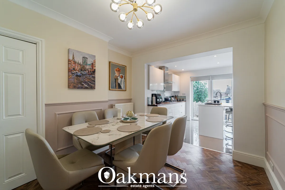 Contemporary dining room with cream marble table, beige upholstered chairs, wainscoting, and open-plan kitchen view with