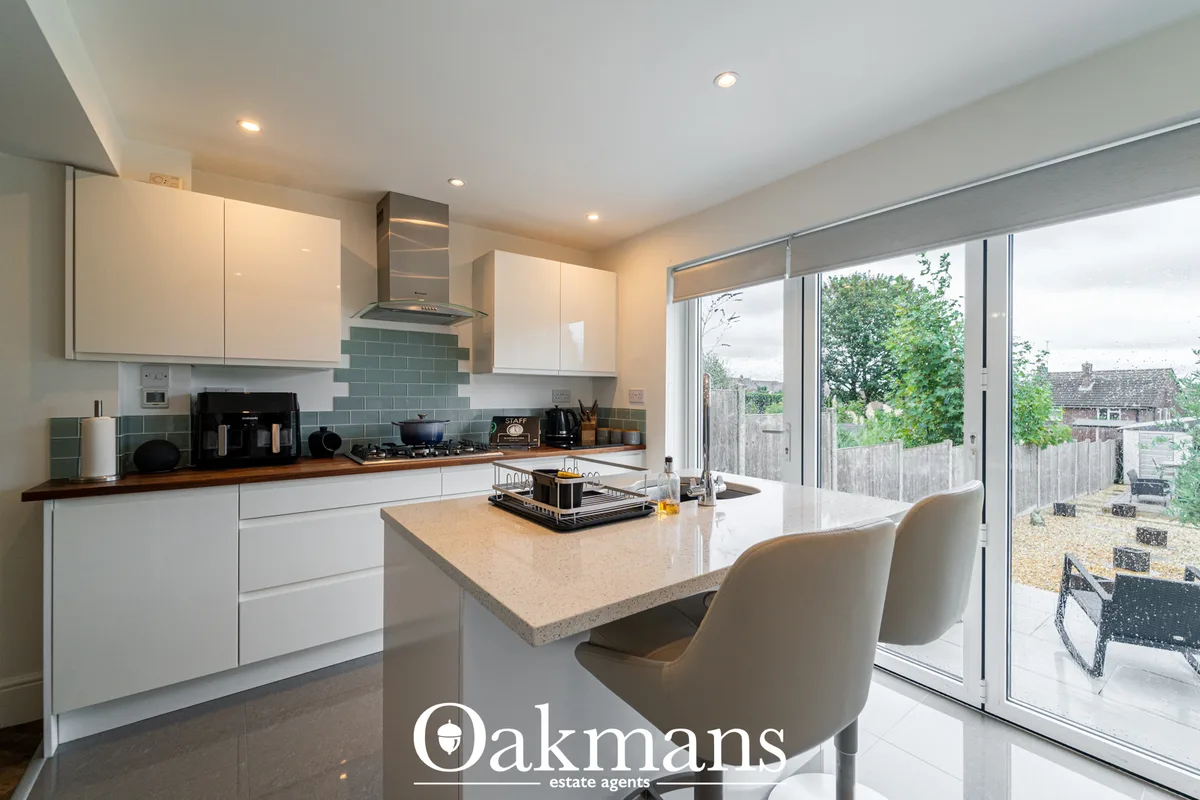 Modern fitted kitchen with white cabinetry, wood worktops, teal subway tile splashback, island with breakfast bar, and s