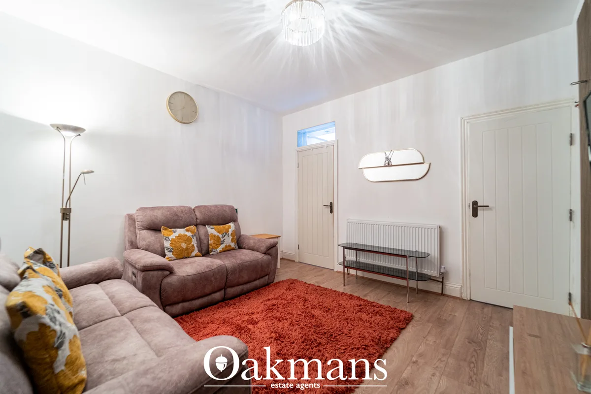 Bright living room with mauve sofa, orange rug, wooden flooring, wall mirror, clock, ceiling light, and multiple doors