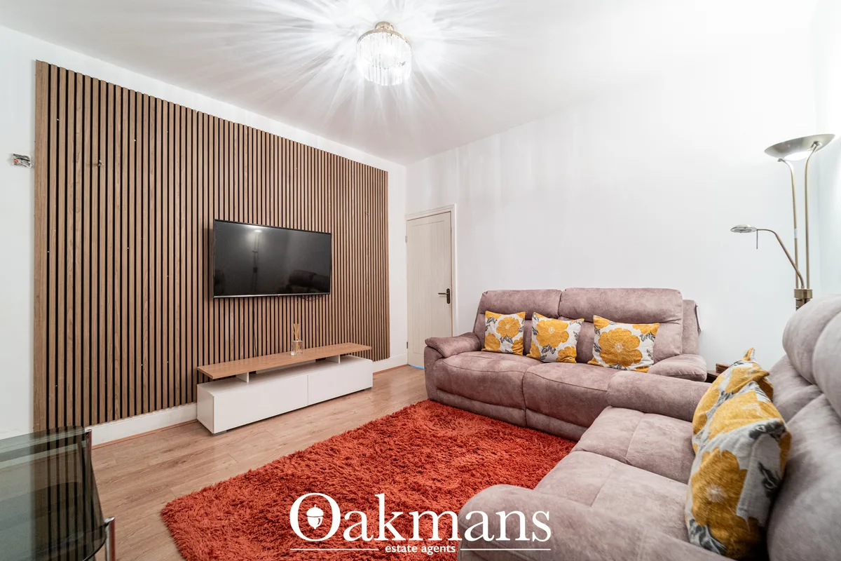 Modern living room with mauve corner sofa, yellow patterned cushions, wooden TV wall with vertical slats, red area rug, 