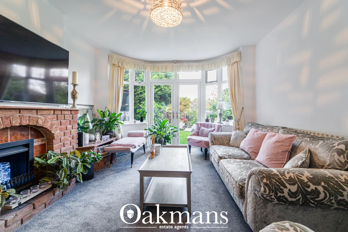 Bright living room with patterned sofa, fireplace, bay windows with cream curtains overlooking garden, ceiling pendant l