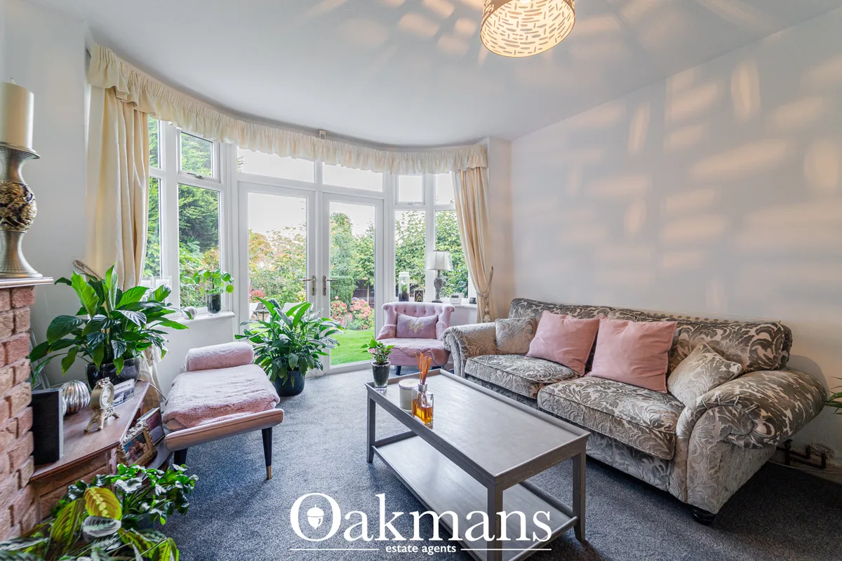 Bright living room with curved bay windows, patterned sofa, pink cushions, coffee table, fireplace and garden views