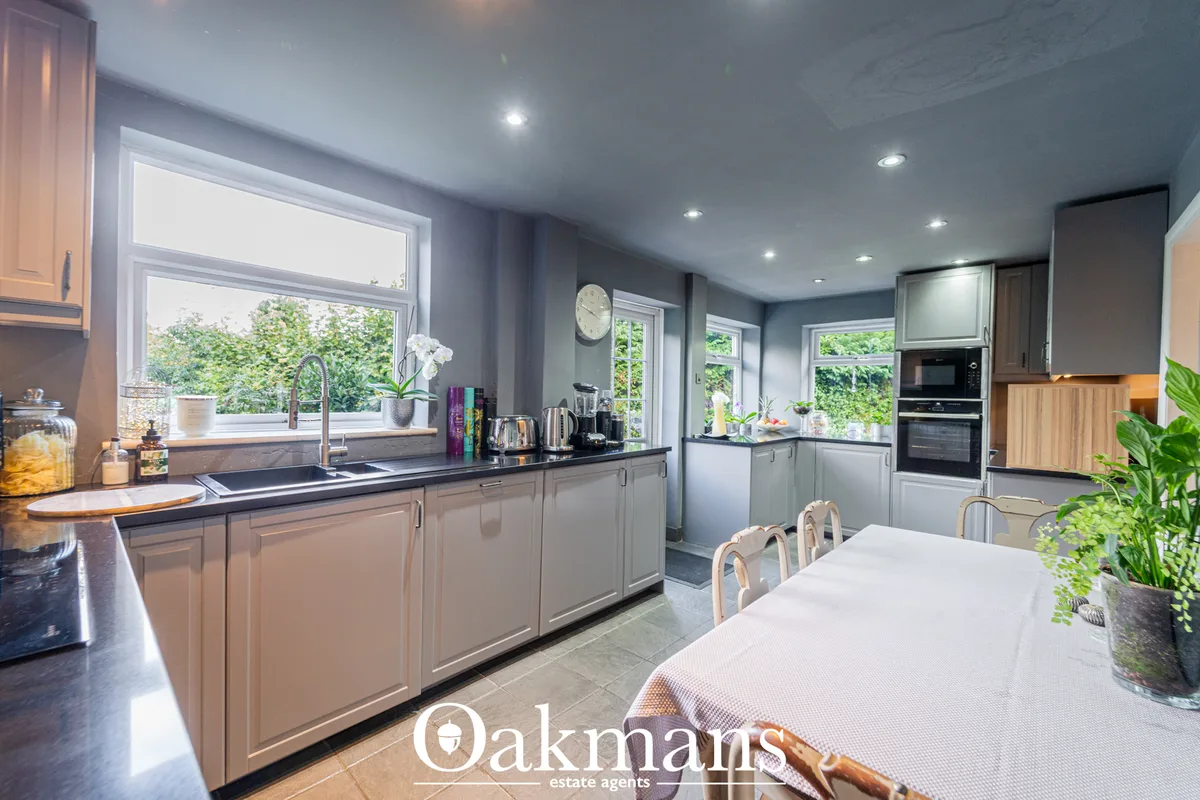 Modern kitchen with grey cabinetry, black worktops, integrated appliances, white dining table, multiple windows overlook