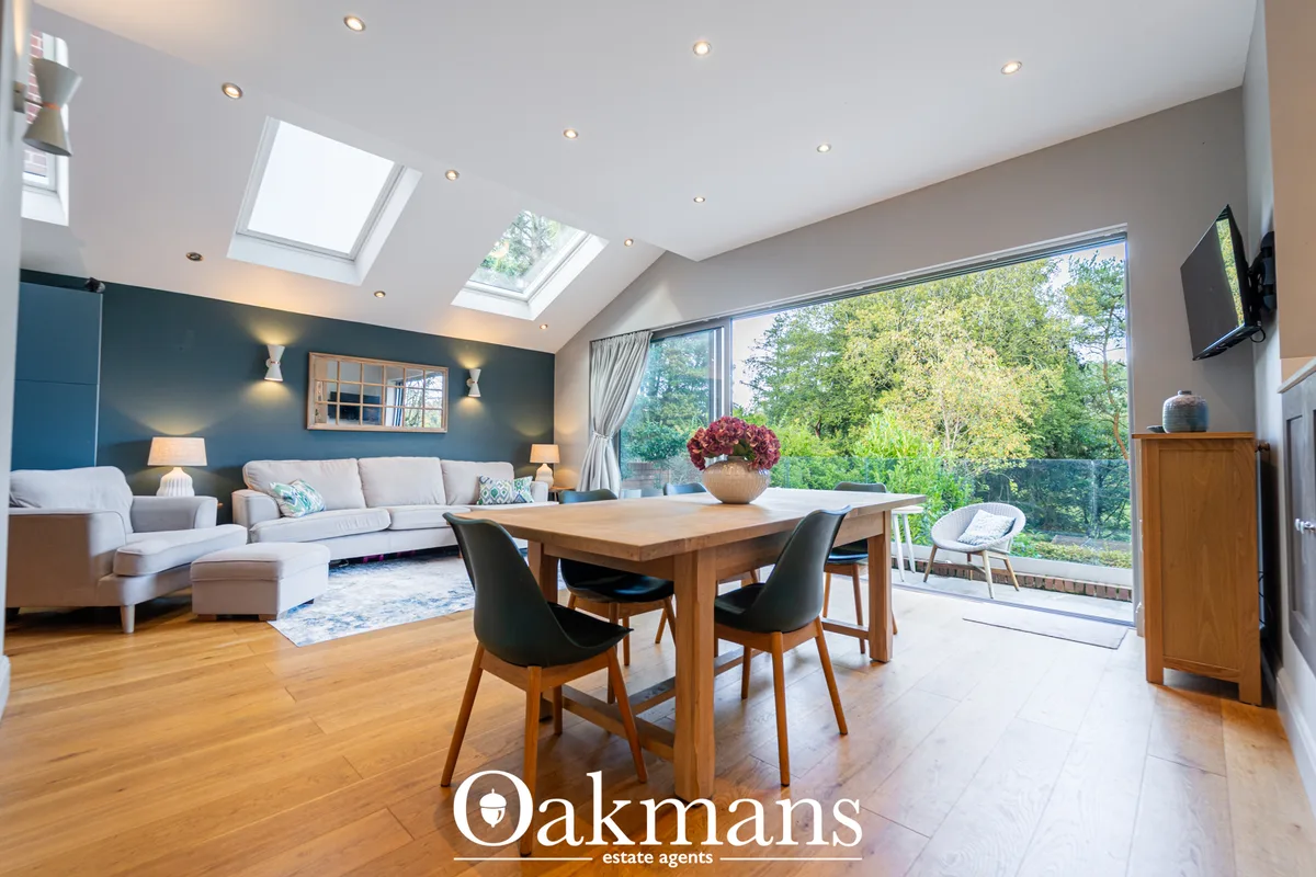 Open-plan living and dining room with grey sofa, wooden dining table, skylight windows, feature dark blue wall, wood flo