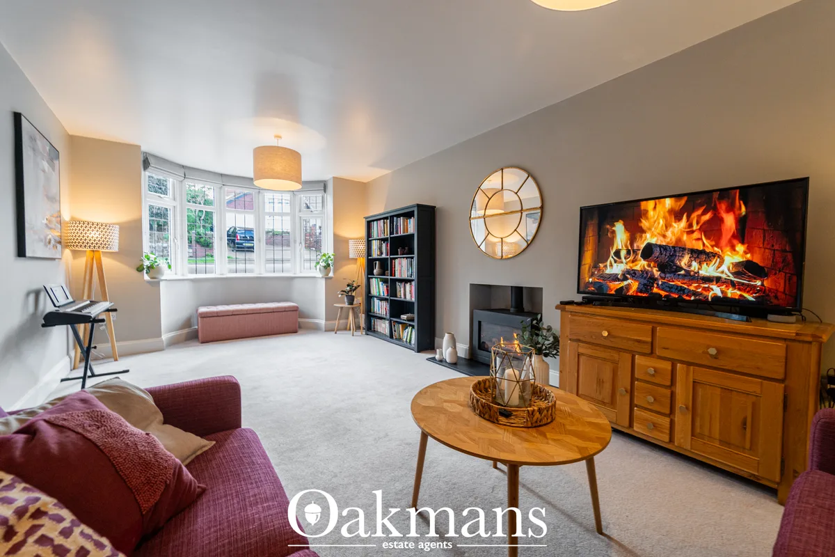 Spacious living room with burgundy armchairs, wooden coffee table, fireplace display on TV, bay windows, bookshelf, pend
