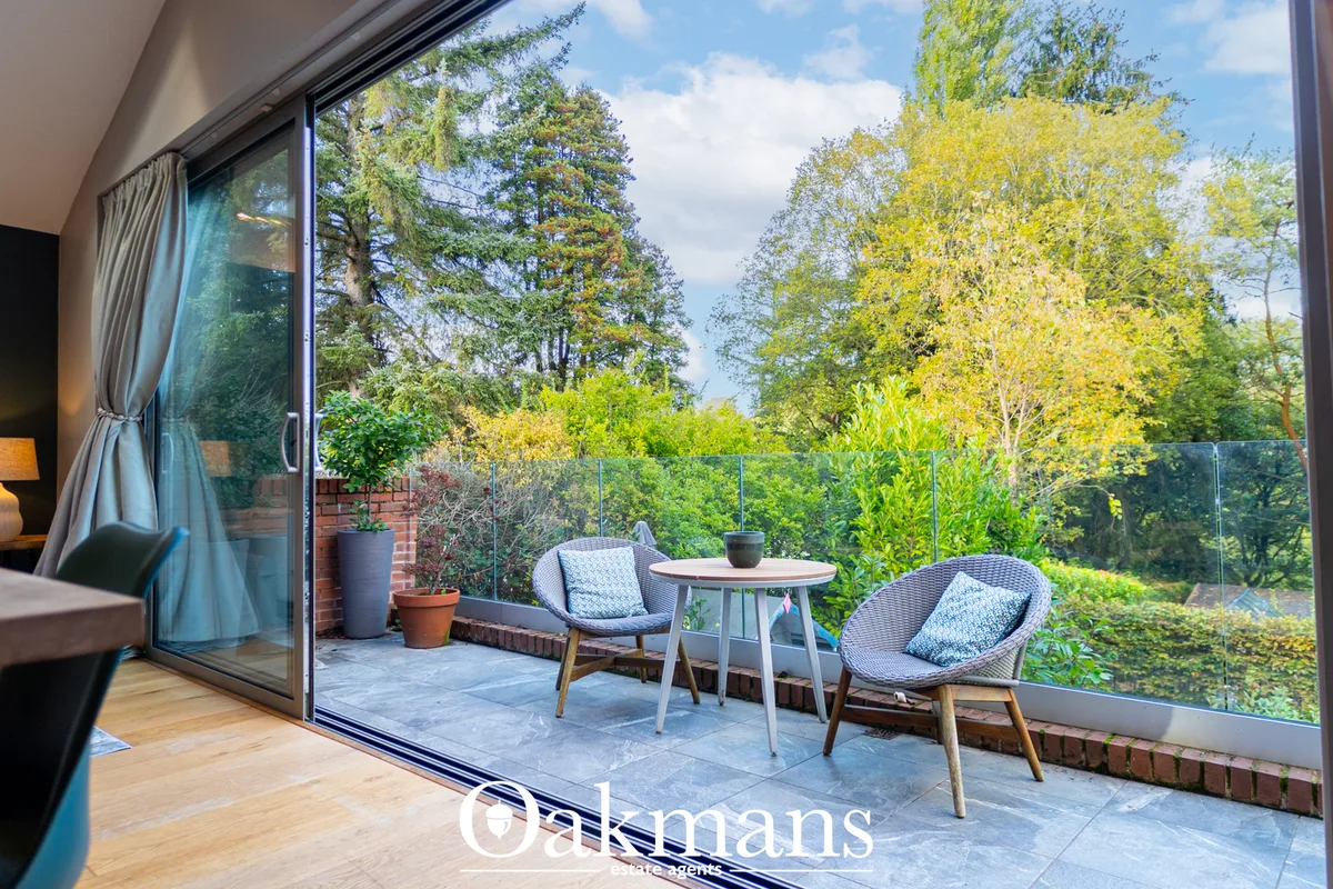 Glass-roofed conservatory with slate paving, two woven chairs, round table, and views over mature gardens and woodland