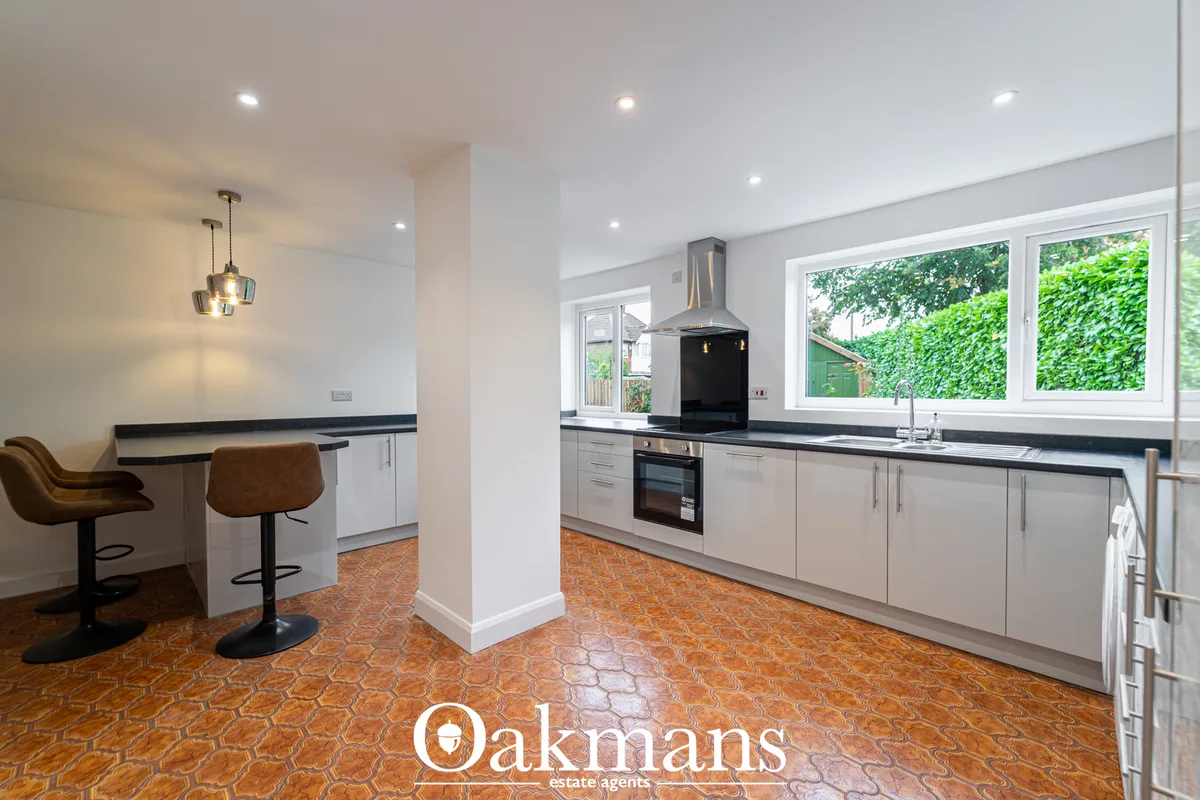 Modern fitted kitchen with white units, black worktops, built-in oven, range hood, multiple windows overlooking garden, 