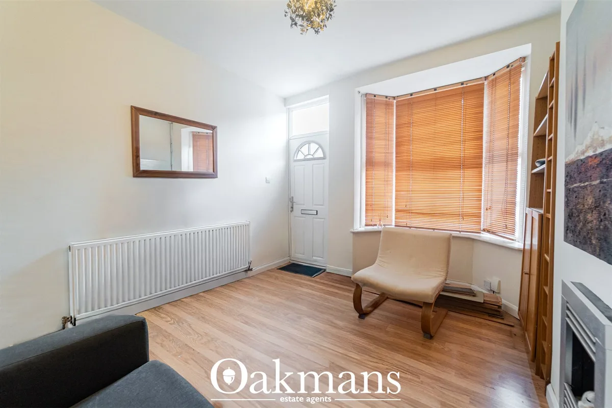 Bright entrance hallway with cream walls, wooden flooring, white radiator, framed mirror, and bay window with wooden bli