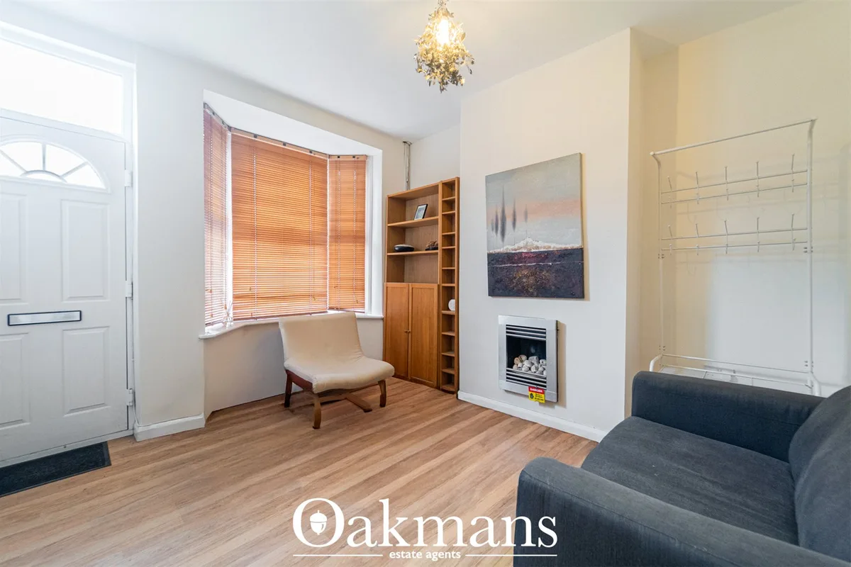 Bright living room with cream walls, dark sofa, beige armchair, wooden shelving unit, framed artwork, fireplace with ins