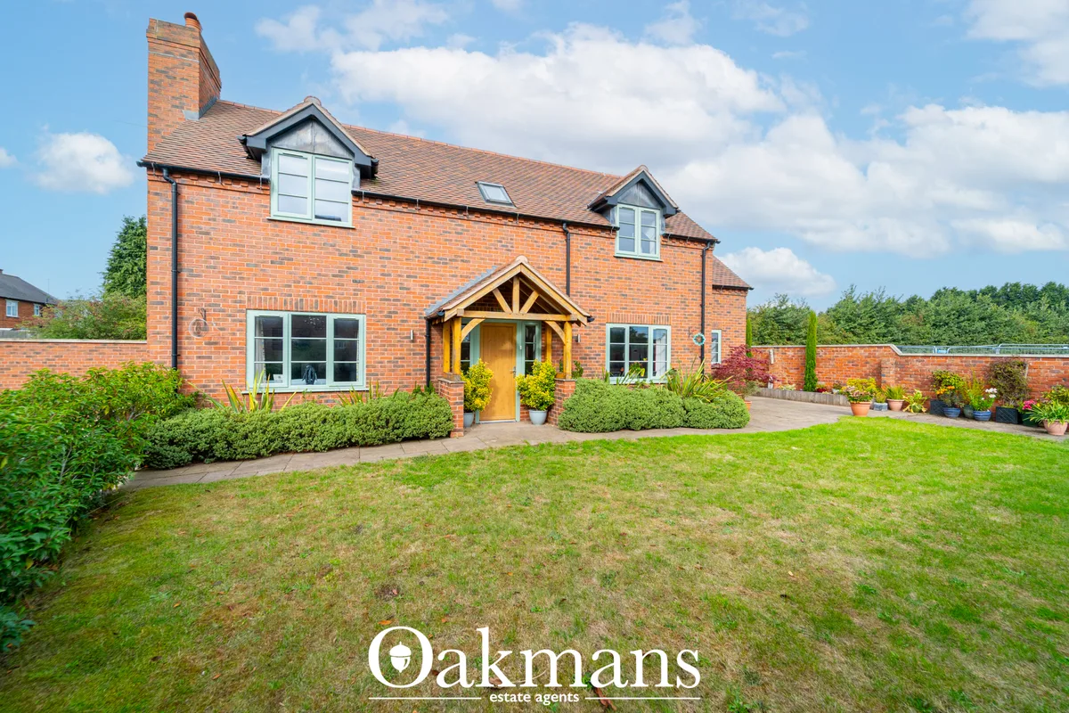 Red brick two-storey family home with timber porch, dormer windows, manicured front garden, lawn and brick boundary wall