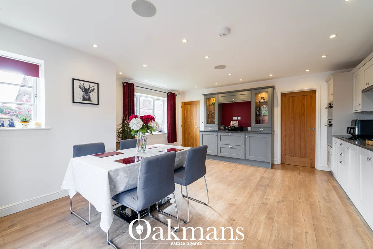 Modern open-plan kitchen with white units, grey cabinetry, dining table with blue chairs, wooden doors and flooring, rec