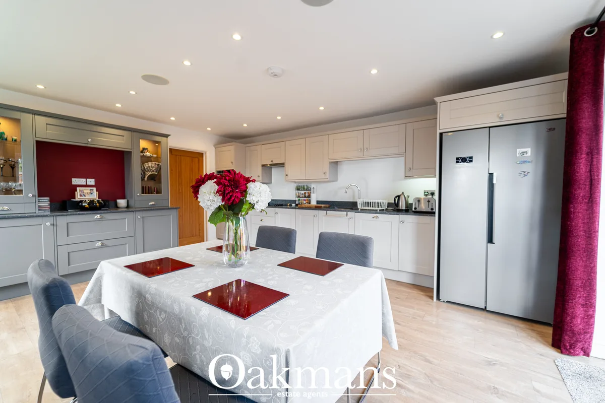 Open-plan kitchen-diner with round white tablecloth table, grey chairs, white cabinetry, burgundy accents and recessed l