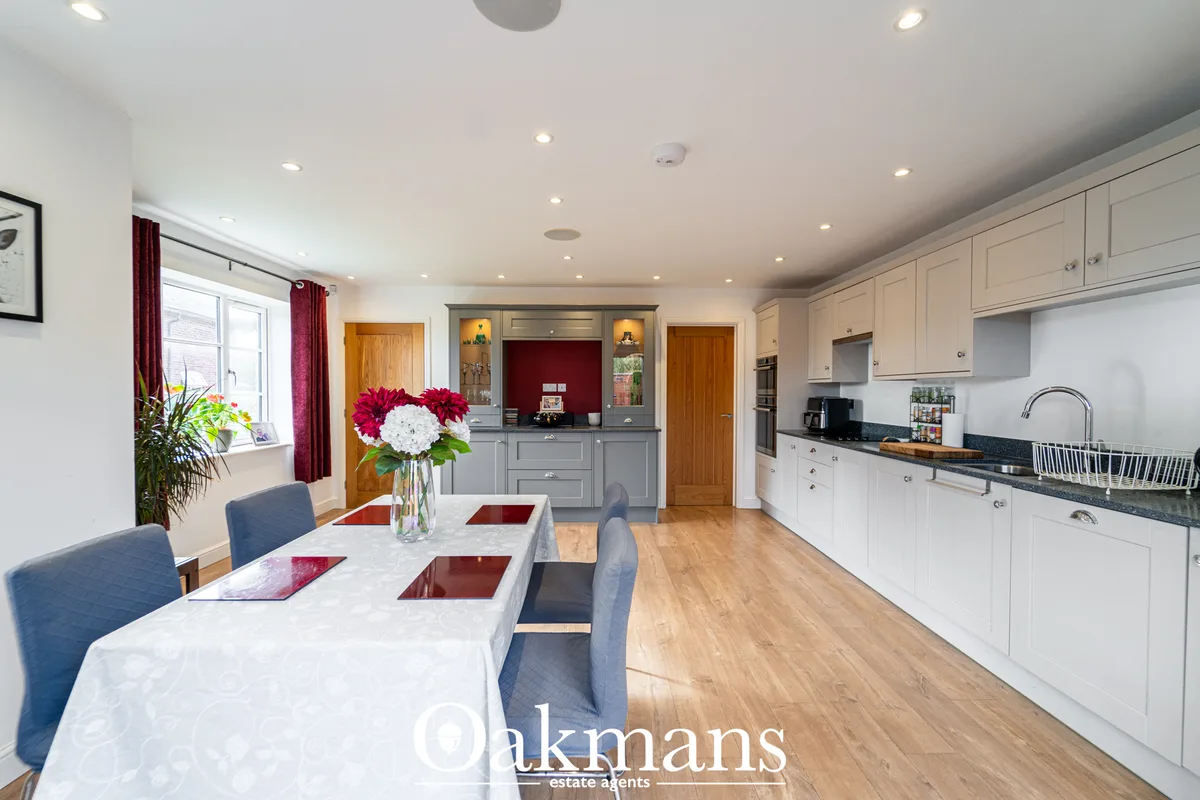 Modern open-plan kitchen with white cabinetry, black granite worktops, breakfast bar, dining table with blue chairs, and